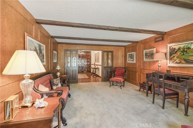 sitting room featuring beamed ceiling, light colored carpet, wooden walls, and french doors