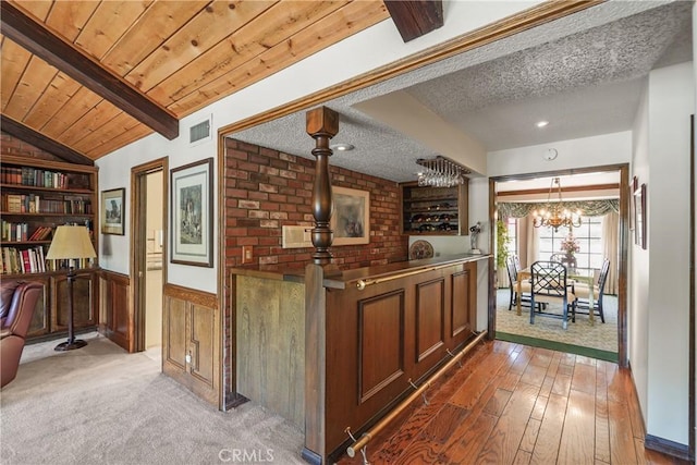 bar featuring an inviting chandelier, hanging light fixtures, hardwood / wood-style flooring, vaulted ceiling with beams, and a textured ceiling