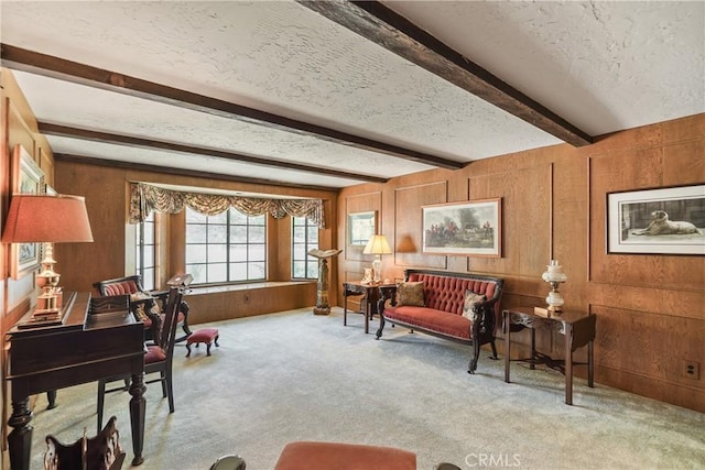 sitting room with wood walls, beamed ceiling, light carpet, and a textured ceiling