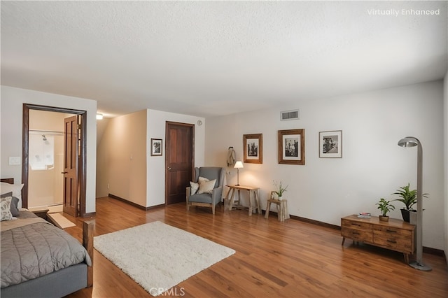 bedroom with visible vents, a textured ceiling, baseboards, and wood finished floors