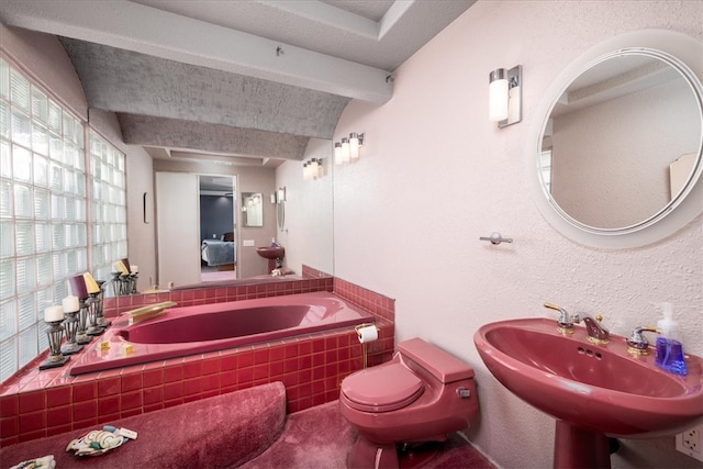 bathroom featuring beam ceiling, sink, toilet, and tiled tub