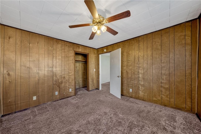 unfurnished bedroom featuring wood walls, ceiling fan, and light colored carpet