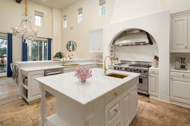 kitchen with an island with sink, light stone countertops, stainless steel appliances, sink, and range hood