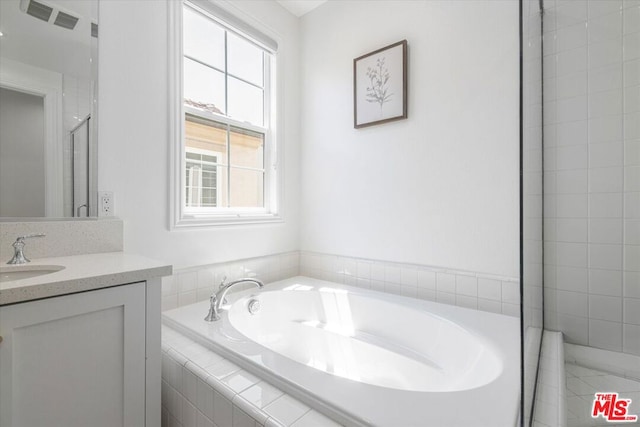 bathroom with tiled bath, plenty of natural light, and vanity