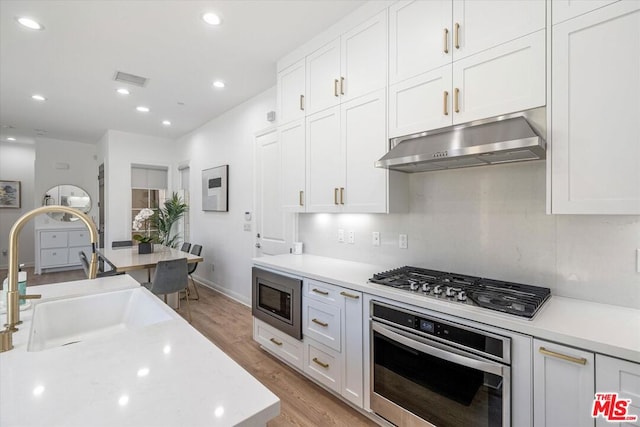 kitchen with appliances with stainless steel finishes, light hardwood / wood-style flooring, white cabinetry, and sink