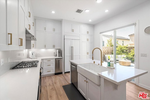 kitchen featuring appliances with stainless steel finishes, light hardwood / wood-style floors, white cabinets, and a kitchen island with sink