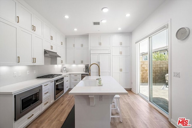 kitchen with white cabinetry, light hardwood / wood-style flooring, built in appliances, and an island with sink