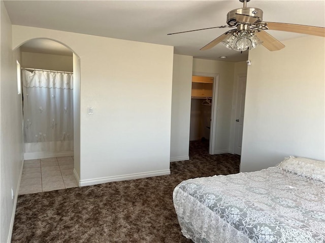 bedroom featuring a closet, a walk in closet, arched walkways, carpet, and baseboards