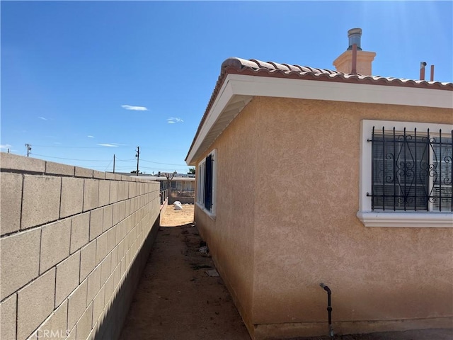 view of property exterior with stucco siding, fence, and a chimney
