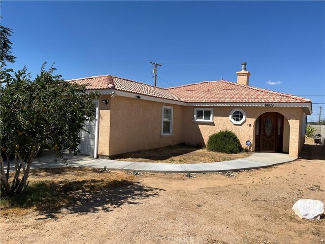 back of property featuring an attached garage, a tiled roof, a chimney, and stucco siding