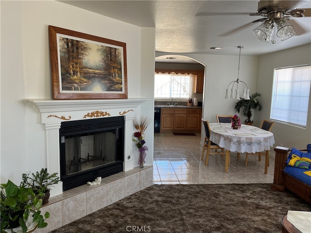 carpeted dining space with sink, a textured ceiling, a fireplace, and ceiling fan