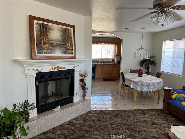 living room featuring a ceiling fan, light tile patterned floors, arched walkways, light carpet, and a tile fireplace