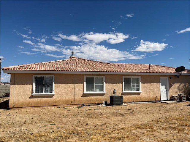 back of property with stucco siding, a tile roof, and central AC