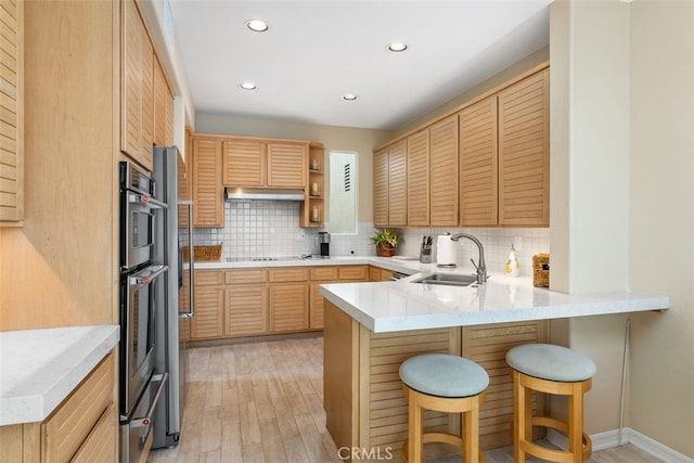 kitchen featuring kitchen peninsula, backsplash, sink, light brown cabinets, and light hardwood / wood-style flooring