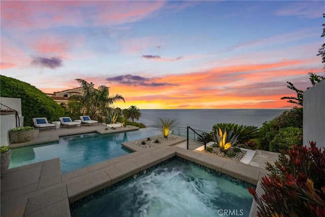 pool at dusk with a jacuzzi and a water view