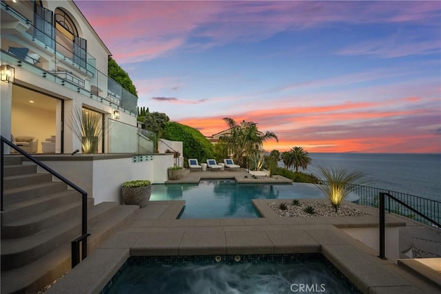 pool at dusk with a patio area, a water view, and an in ground hot tub