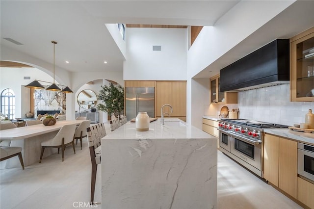 kitchen featuring light stone countertops, custom range hood, high end appliances, sink, and pendant lighting