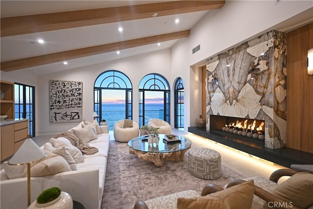 living room with lofted ceiling with beams, a water view, and a stone fireplace