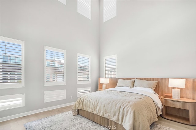 bedroom featuring light wood-type flooring and a towering ceiling