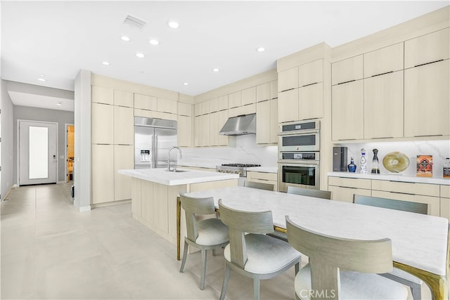 kitchen featuring stainless steel appliances, a center island with sink, a kitchen bar, and ventilation hood