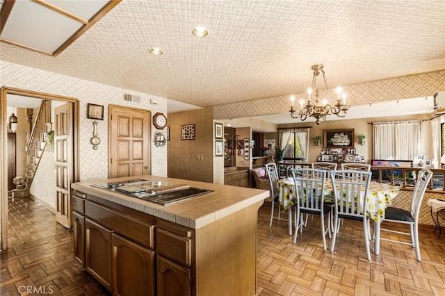 kitchen featuring dark brown cabinetry, pendant lighting, stainless steel gas cooktop, a chandelier, and light parquet floors