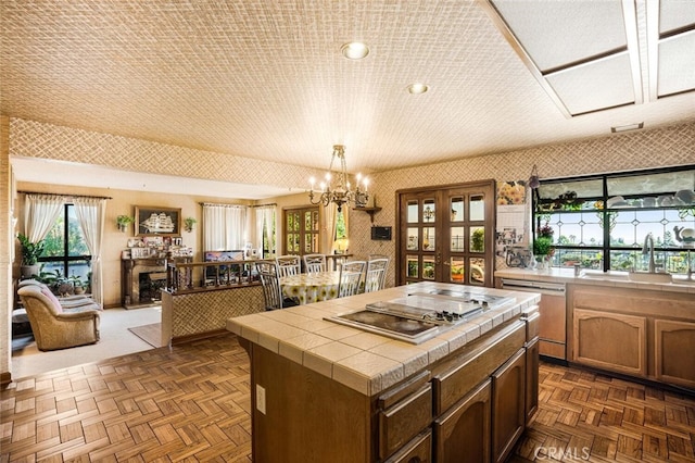 kitchen with hanging light fixtures, a kitchen island, stainless steel appliances, tile counters, and sink