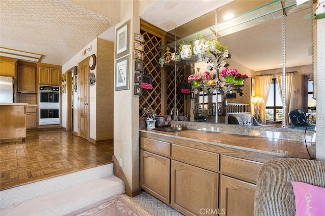 bar with light parquet floors, a textured ceiling, double oven, and sink