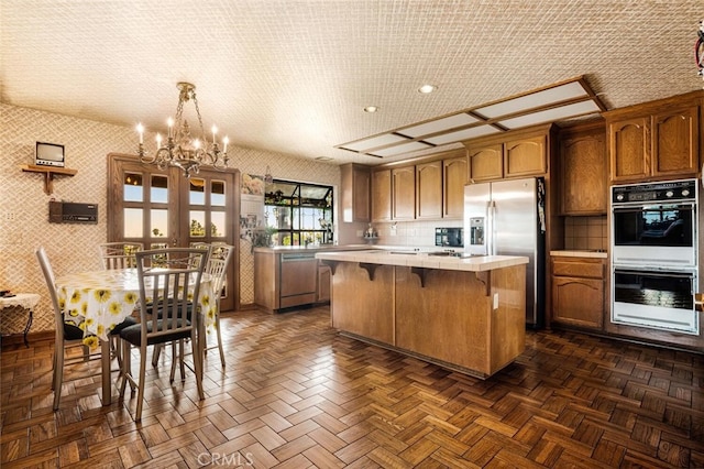 kitchen with dark parquet flooring, stainless steel appliances, a center island, decorative light fixtures, and a chandelier