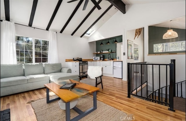 living room featuring beamed ceiling, light hardwood / wood-style flooring, sink, high vaulted ceiling, and a skylight