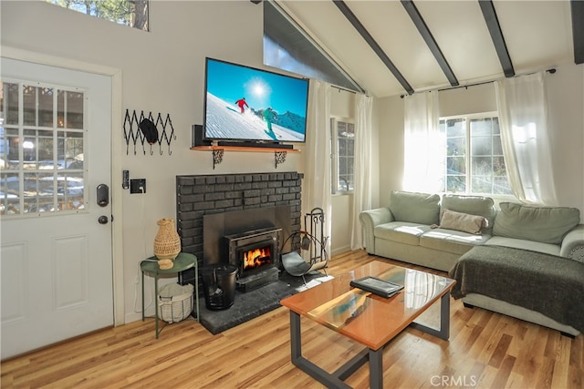 living room with a wealth of natural light, beam ceiling, light hardwood / wood-style flooring, and a brick fireplace