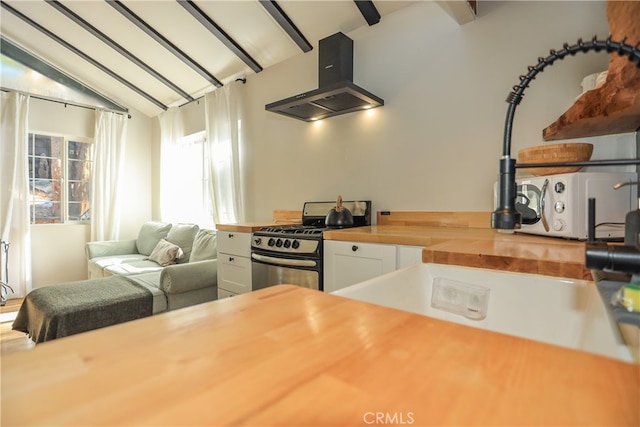 kitchen featuring island range hood, butcher block counters, vaulted ceiling with beams, stainless steel range with gas cooktop, and white cabinetry