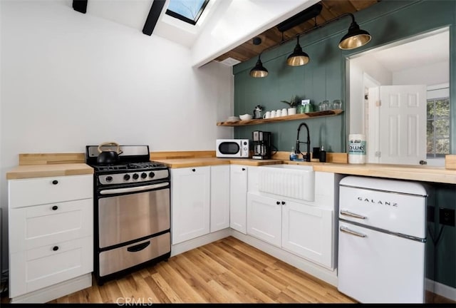 kitchen featuring white cabinets, butcher block counters, decorative light fixtures, and stainless steel range with gas stovetop