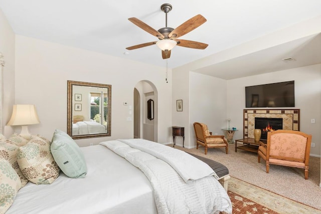 bedroom featuring carpet flooring, ceiling fan, and a tiled fireplace