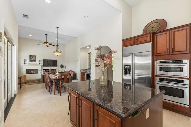 kitchen featuring a center island, built in fridge, ceiling fan, dark stone countertops, and decorative light fixtures