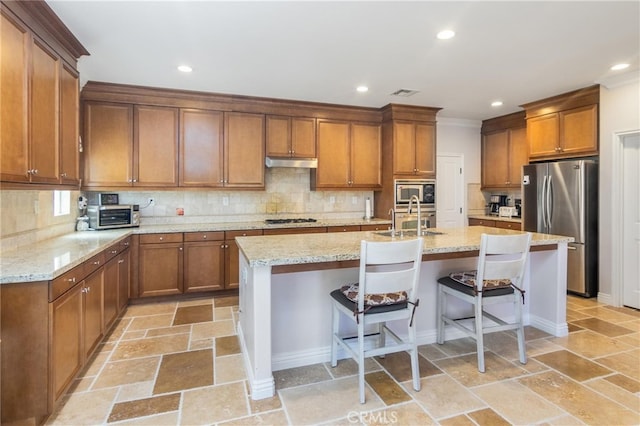 kitchen with a kitchen bar, tasteful backsplash, stainless steel appliances, a kitchen island with sink, and sink