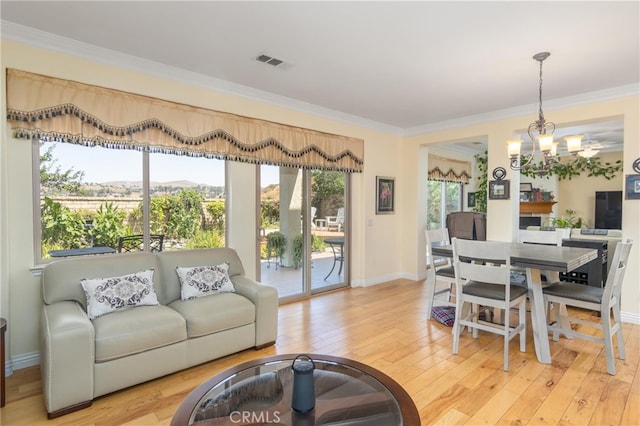 living room with crown molding, an inviting chandelier, and light wood-type flooring