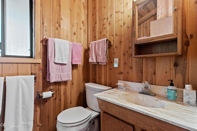 bathroom with vanity, wood walls, and toilet