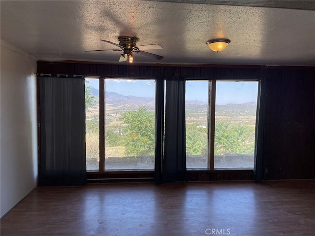 empty room with ceiling fan, a mountain view, a healthy amount of sunlight, and hardwood / wood-style floors