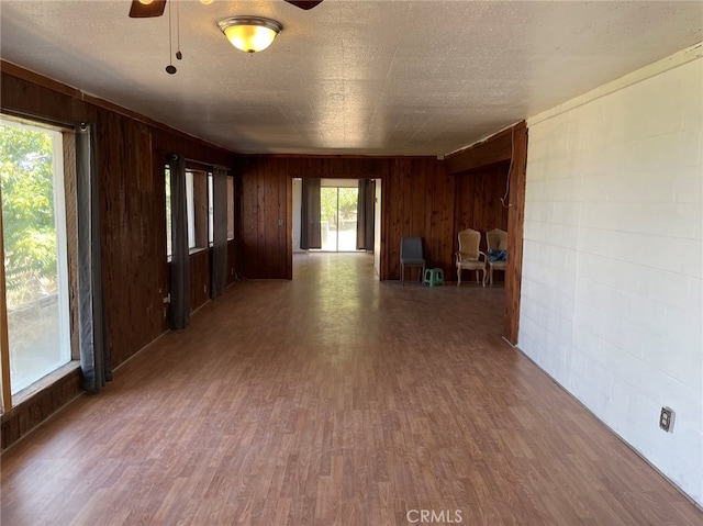 empty room with a textured ceiling, wooden walls, dark wood-type flooring, and ceiling fan