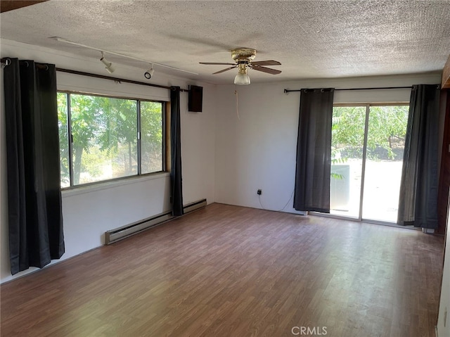 unfurnished room featuring a baseboard radiator, a textured ceiling, wood-type flooring, and a healthy amount of sunlight