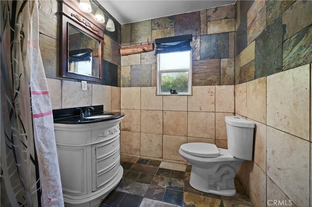 bathroom with vanity, toilet, and tile walls