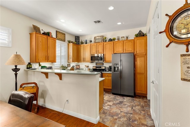 kitchen featuring kitchen peninsula, stainless steel appliances, dark wood-type flooring, and a breakfast bar area