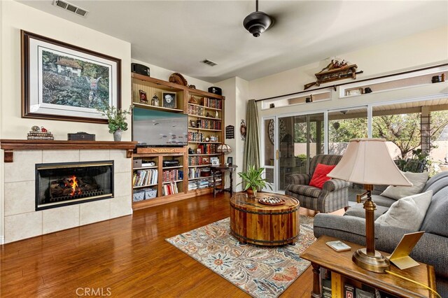 living room featuring a tile fireplace, dark hardwood / wood-style flooring, and ceiling fan