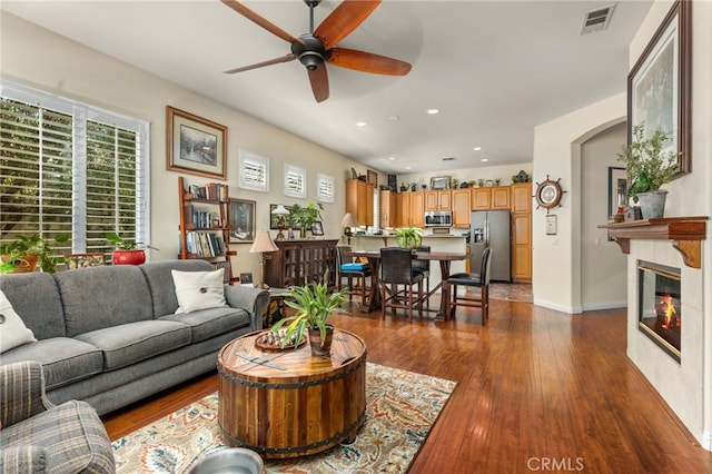 living room with a tiled fireplace, ceiling fan, and dark hardwood / wood-style floors