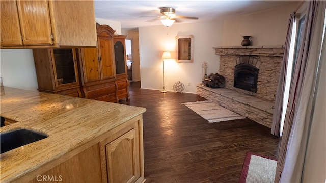 interior space featuring a stone fireplace, ceiling fan, and dark wood-type flooring