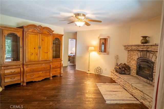 sitting room with a stone fireplace, ceiling fan, and dark hardwood / wood-style flooring