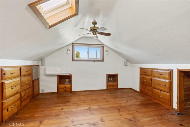 additional living space featuring ceiling fan, light wood-style flooring, lofted ceiling with skylight, and a wall unit AC