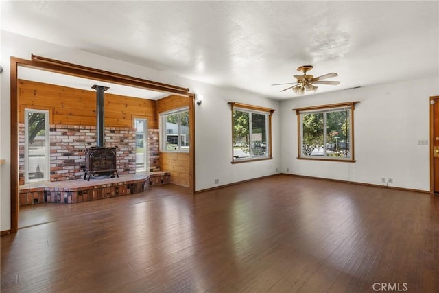 unfurnished living room with a wood stove, baseboards, a ceiling fan, and wood finished floors