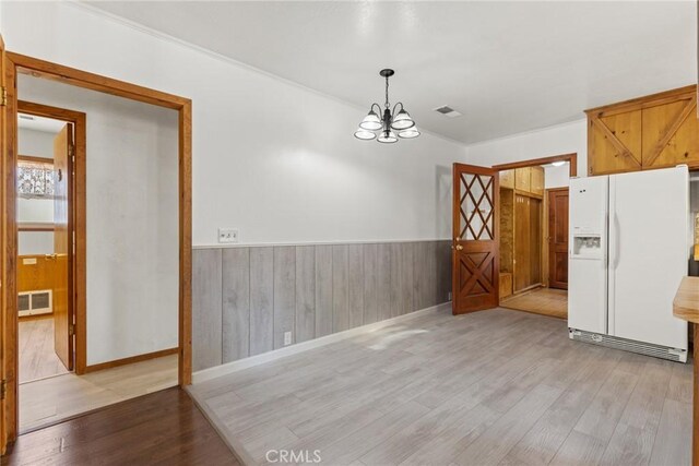 unfurnished dining area with a notable chandelier, wainscoting, visible vents, and wood finished floors