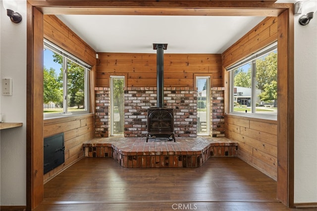 unfurnished living room featuring a wood stove, wooden walls, and dark hardwood / wood-style flooring